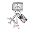 Silver charm with multiple charms including a pink Eiffel Tower, a suitcase, and a heart with a key on a white background.